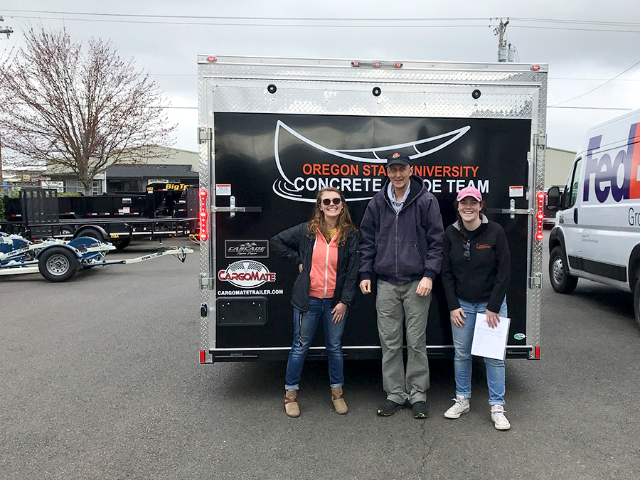 Two students and a professor stand in front of a canoe trailer.