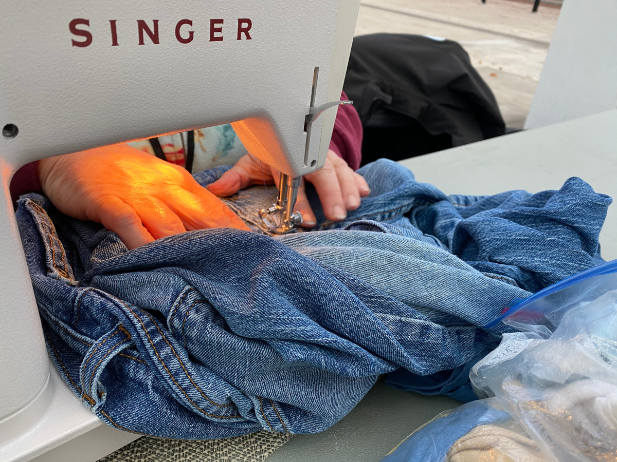 A person using a sewing machine to repair a pair of jeans.