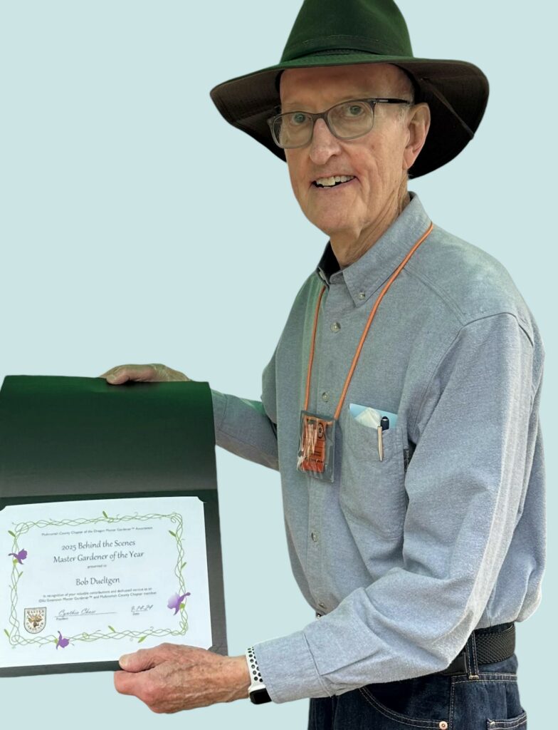 Bob Dueltgen, smiling, wearing a dark brimmed hat, and holding a certificate.