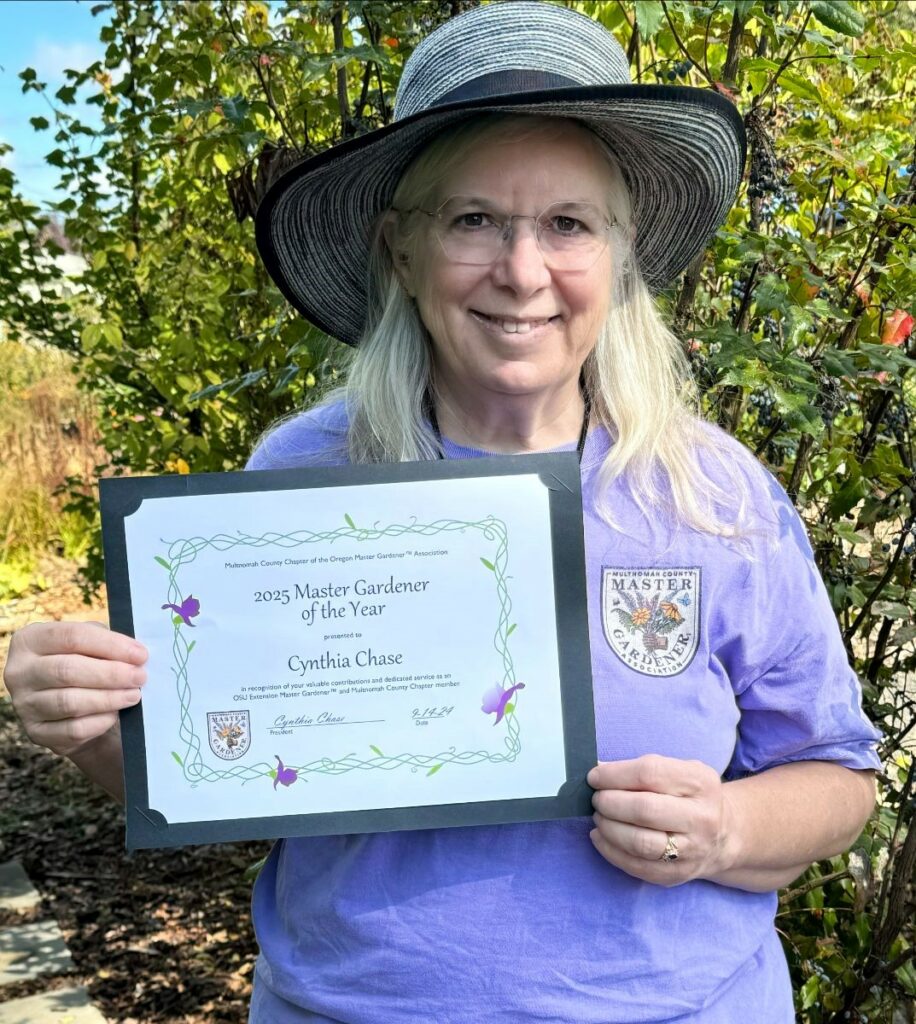 Cynthia Chase smiling, wearing a grey brimmed hat and holding a certificate.