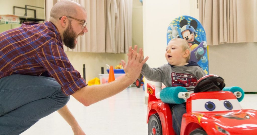 Researcher Sam Logan high-fives a child in a Go Baby Go car