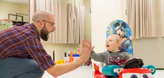 Researcher Sam Logan high-fives a child in a Go Baby Go car