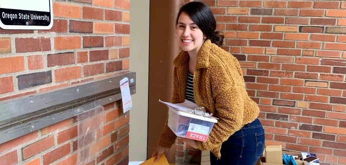Female student in an orange jacket picking up a COVID test kit
