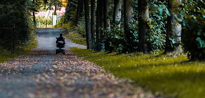 person in wheelchair goes down path of trees, leaves