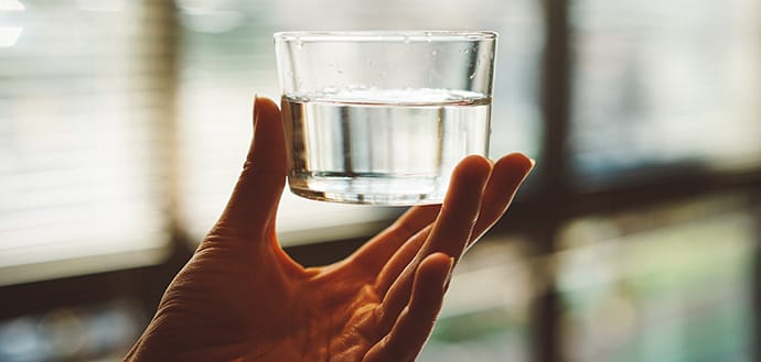 hand holding a small, clear glass of water