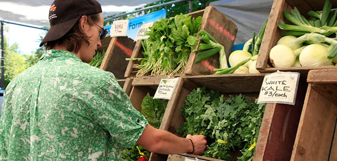 man selects arugula, vegetables while shopping at farmers market