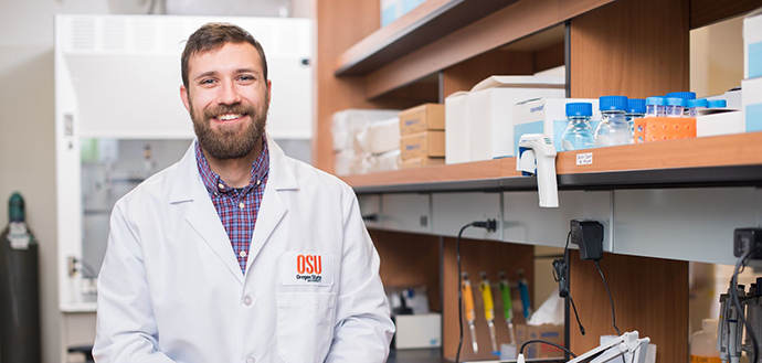Harrison Stierwalt smiles in Oregon State lab coat, laboratory