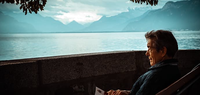 elderly man looks out at lake, mountains