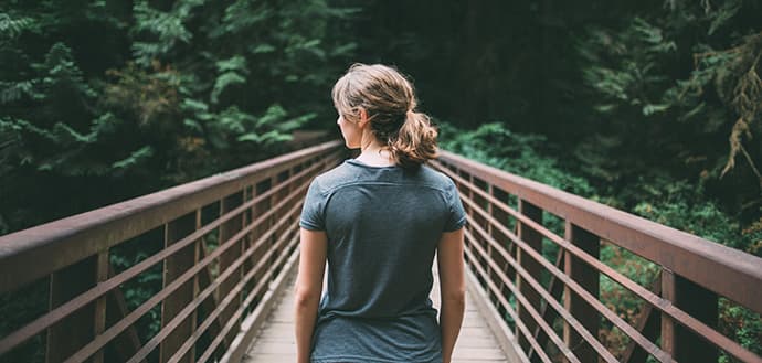 blonde woman stands on bridge, looks at forest
