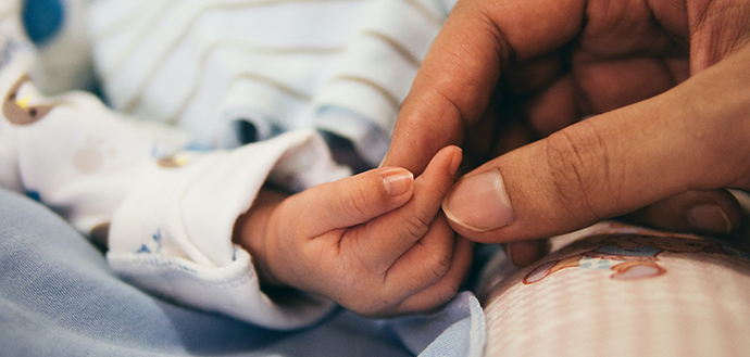 adult holds newborn hand with fingertips