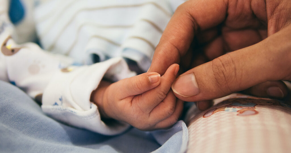 adult holds newborn hand with fingertips