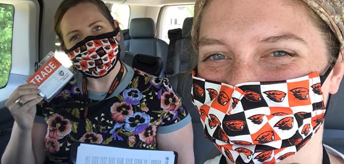 two females wear Oregon State University face masks, hold up TRACE name tags