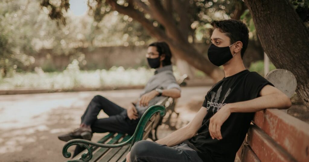 two men wearing masks, sitting on different benches