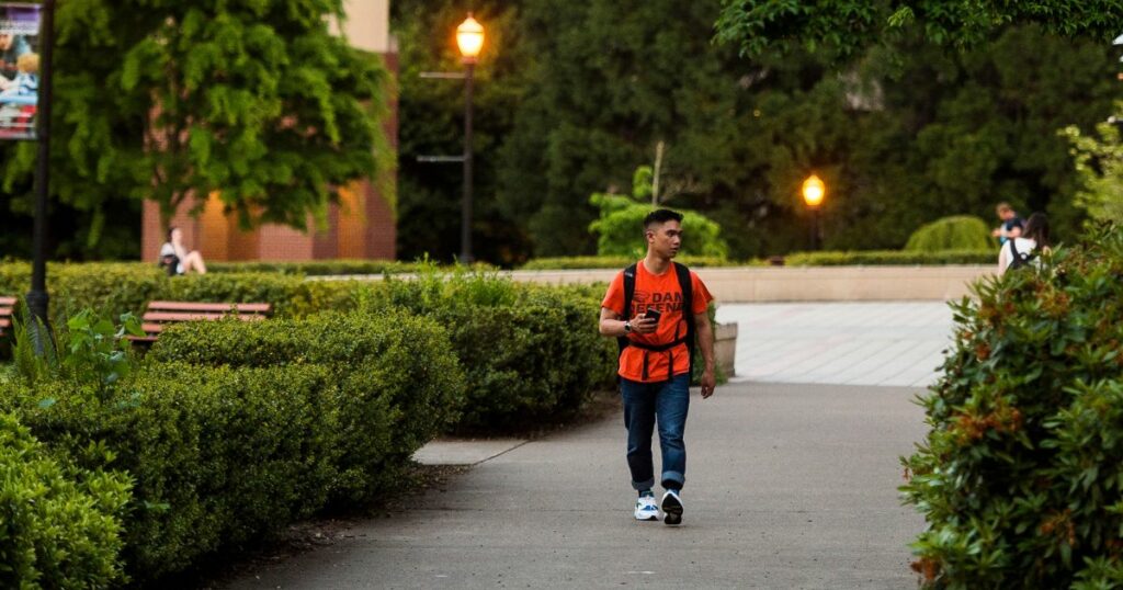 Student in orange t-shirt walking by Oregon State library