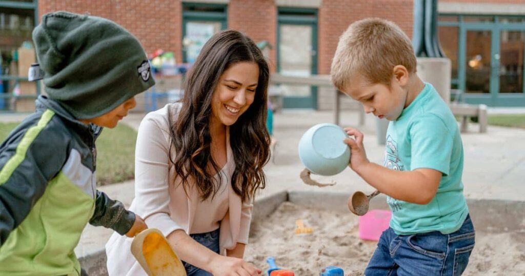 Alexis Merculief, a student in the HDFS PhD program, playing in the sandbox with two children