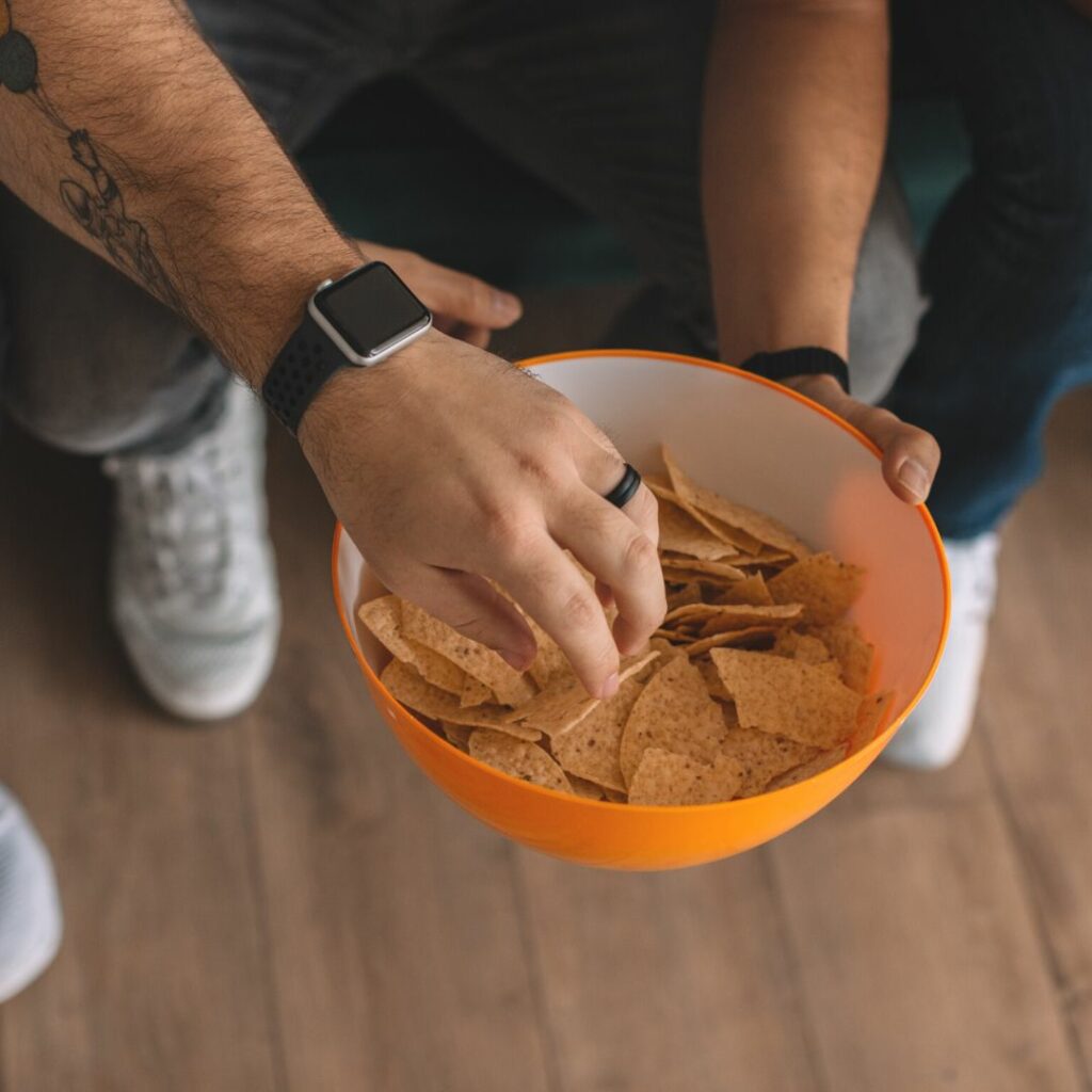 man's hand grabbing a chip out of an orange bowl