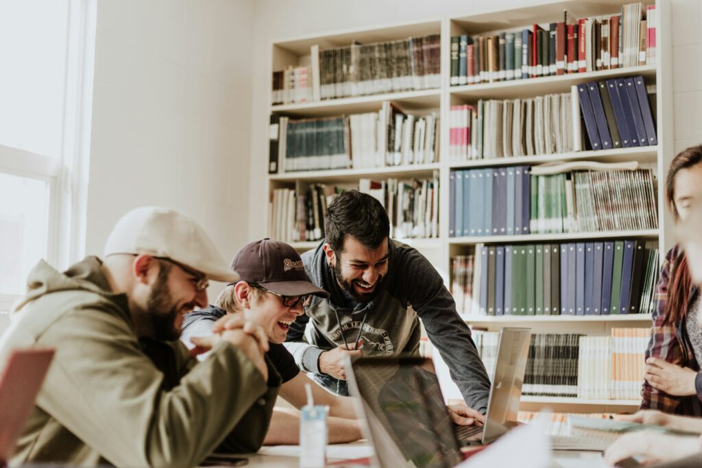 a group of college students working together while looking at their laptops and smiling