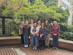 Eight members of a lab group stand on a brick patio, in front of a tree.