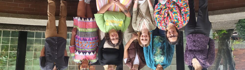 six people stand and three people kneel on a brick patio, smiling at the camera