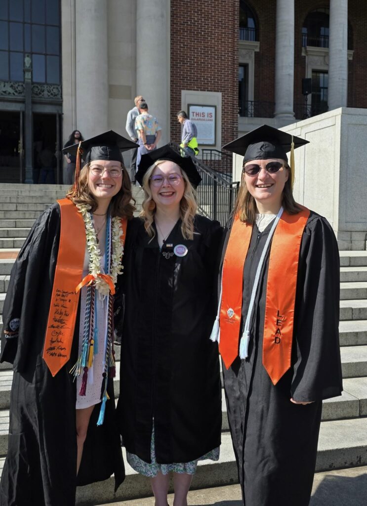 three young women stand in their caps and gowns in front of the Oregon State University memorial union, on graduation day