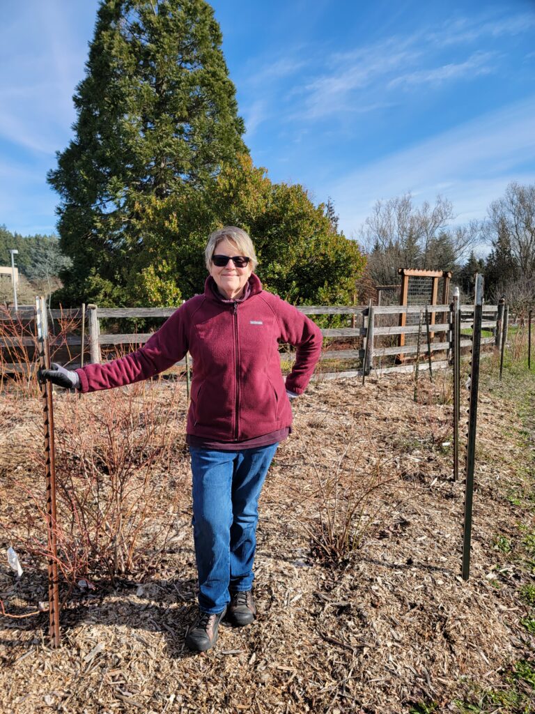 Sue in the garden, wearing sunglasses and gardening gloves, ready to garden.