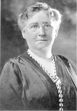 Black and white portrait of white woman with glasses and a patterned necklace.