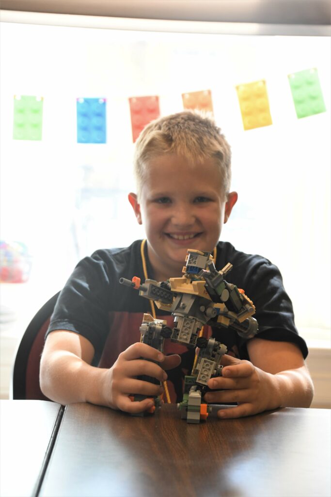 A young boy holding a small LEGO robot he made at 4-h camp.