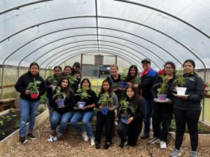 A group of 13 people hold potted plants