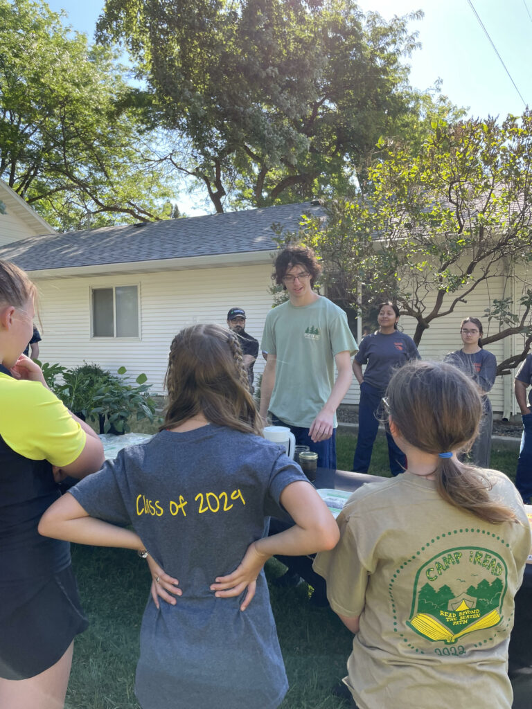 A young man gives an outdoor demonstration while kids watch.