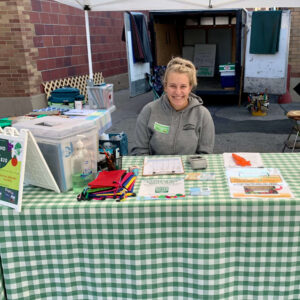 A woman in a gray sweatshirt sits outside at a table covered in a green checked tablecloth