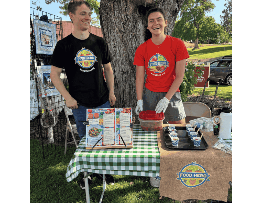 Two people wearing food hero shirts running a table labeled food hero serving salsa.
