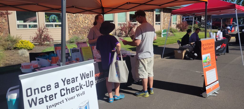 A girl talking to 2 community members infront of a booth outside