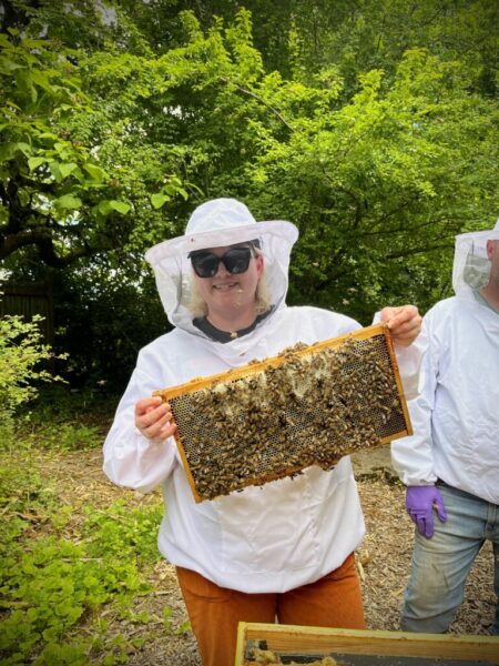 A girl in a bee suit holding a frame from a bee hive covered in wax and bees.