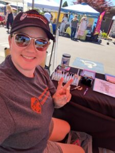A selfie of a girl sitting at a farmers market booth in OSU gear.
