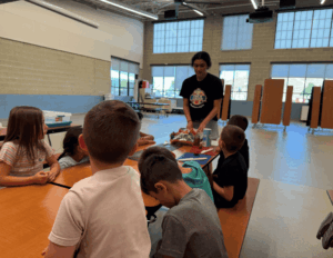 Kids sitting around a table learning about food by a girl in a Food Hero shirt