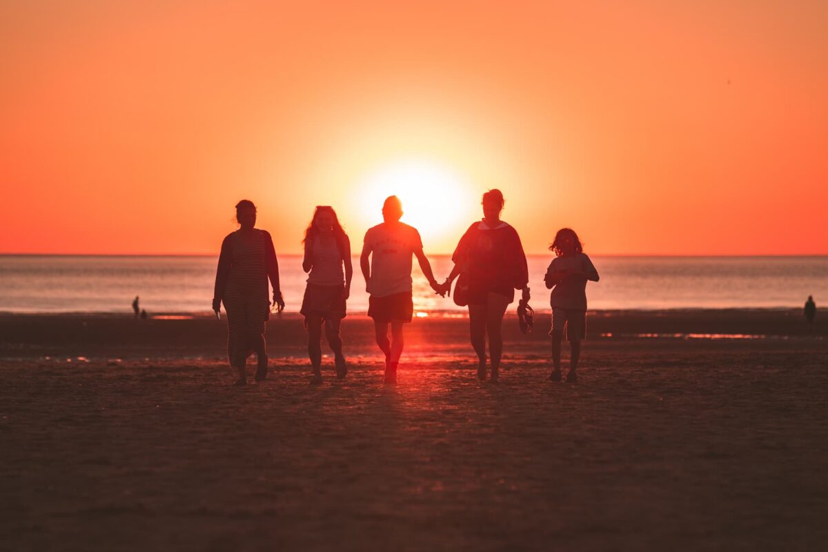 Silhouettes of 5 people walking together at sunset on the coast.