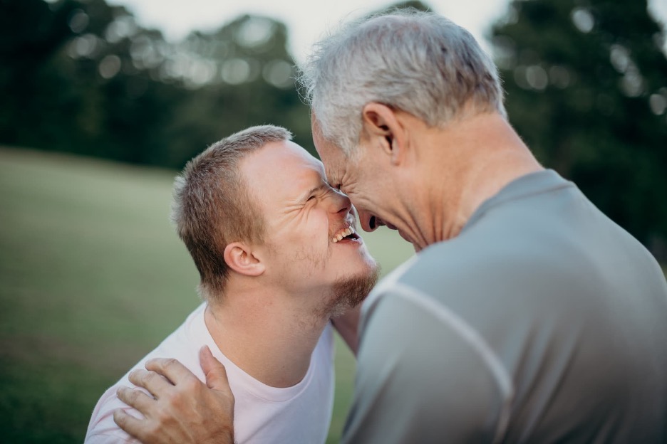 A smiling young adult with Down Syndrome and a smiling older adult.