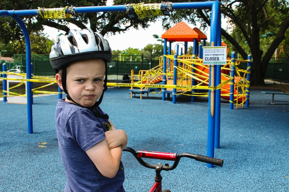 A child crossing their arms and scowling at a closed playground.