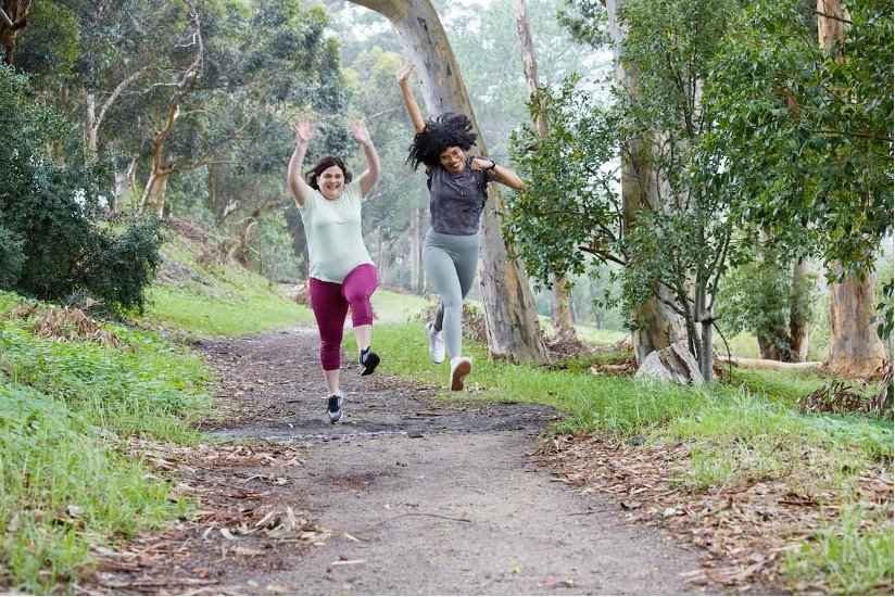 Two people jumping happily on a forest path.