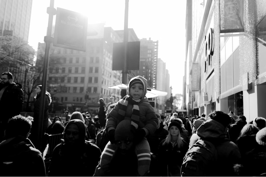 A black and white image of a child getting a shoulder ride on a city street
