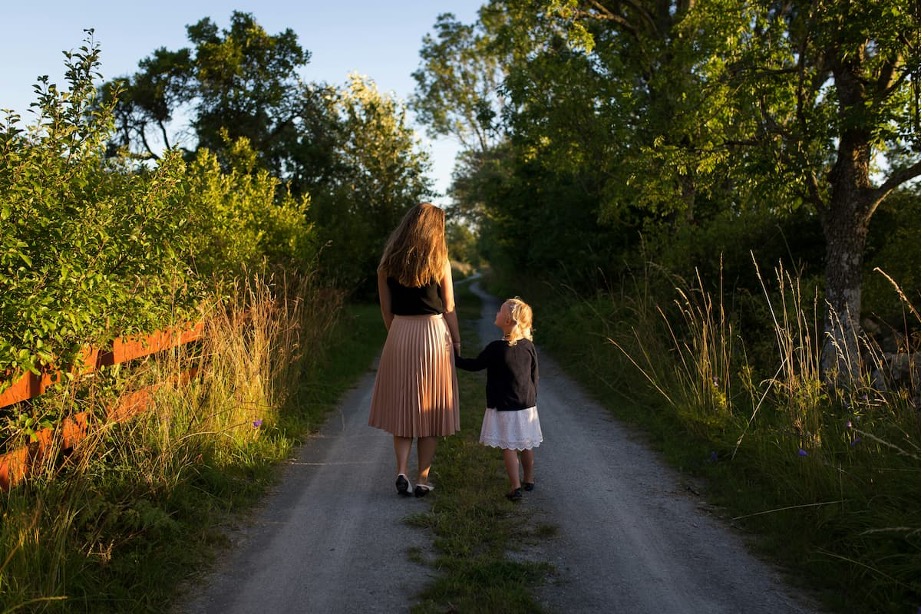An adult and child walking down a nature path, holding hands
