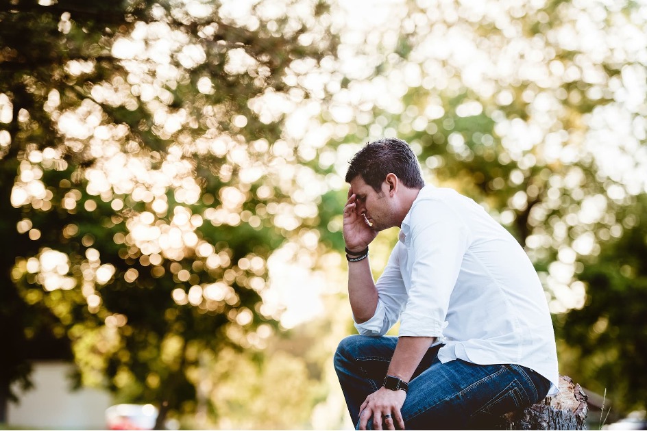 Adult sitting outside with head in their hand.