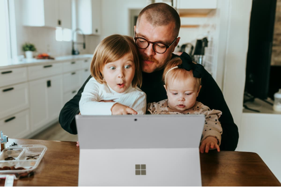 An adult looks at a laptop with two young children