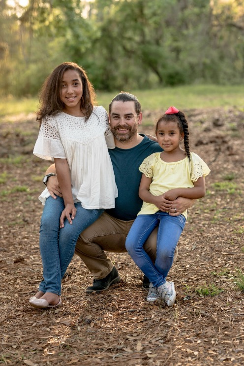 A parent kneels down and balances their two children on their knees.