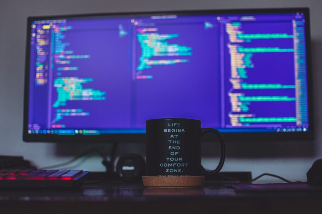 Coffee mug that says "Life begins at the end of your comfort zone" sitting in front of computer monitor.