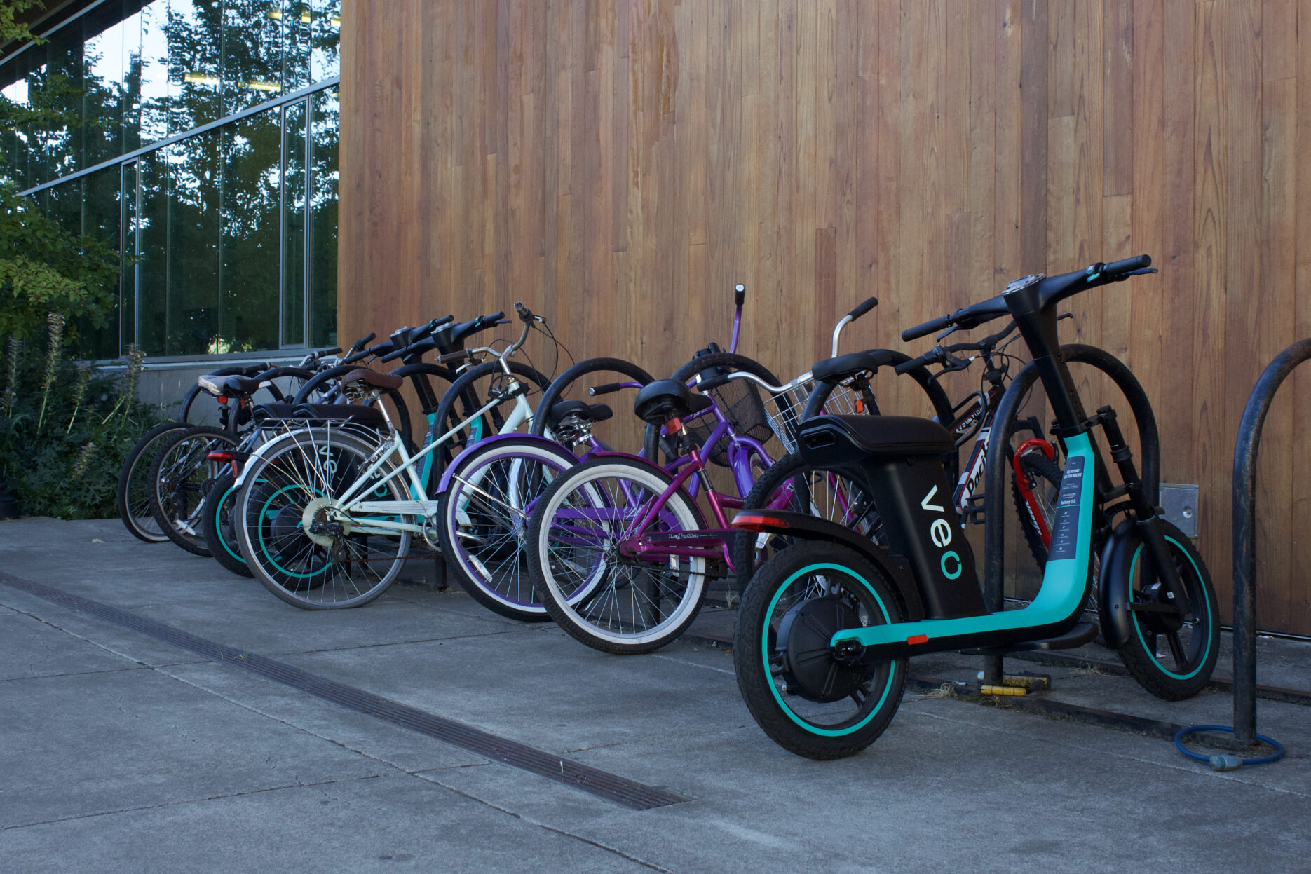 A Veo scooter parked at a bike rack next to a wooden wall.