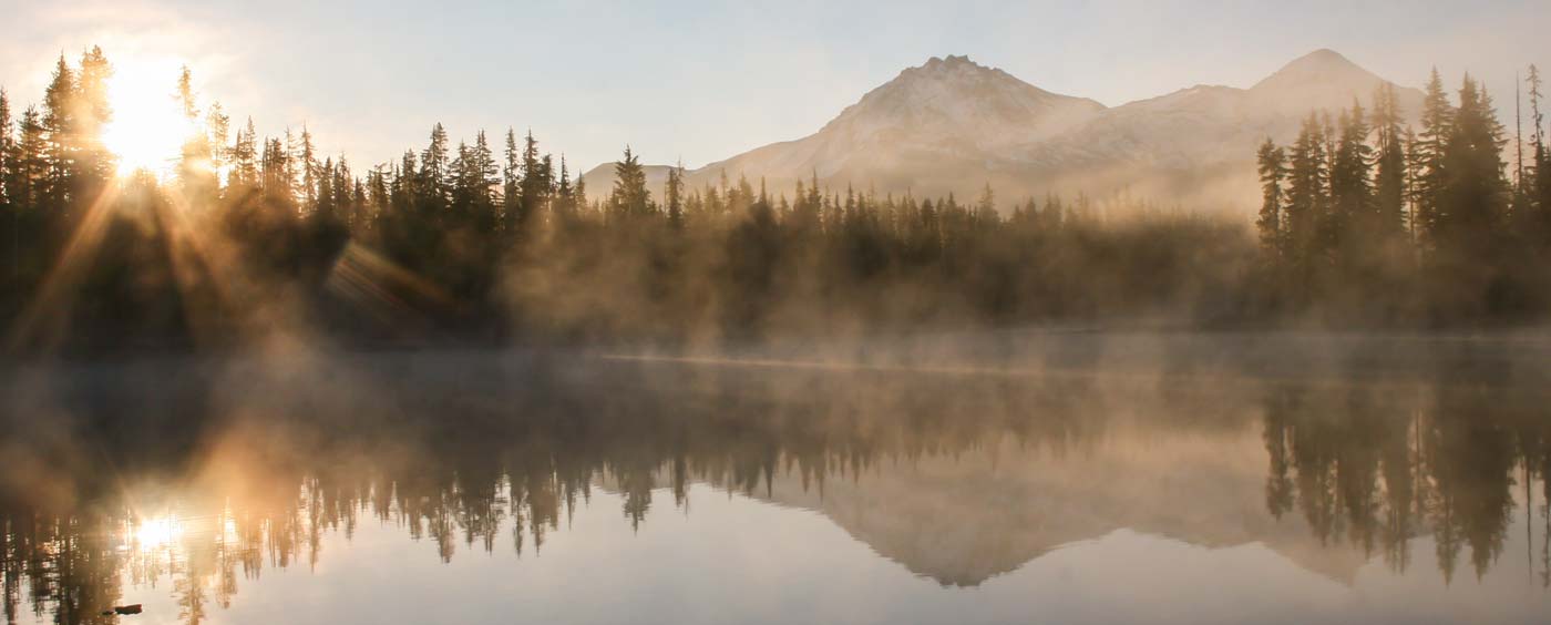 Fog on a lake with peaks and silhouettes of trees lining the shore