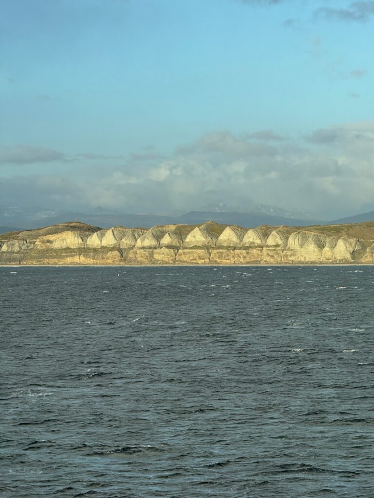 A cliff face of triangular or pyramidal rock formations at the edge of the water.