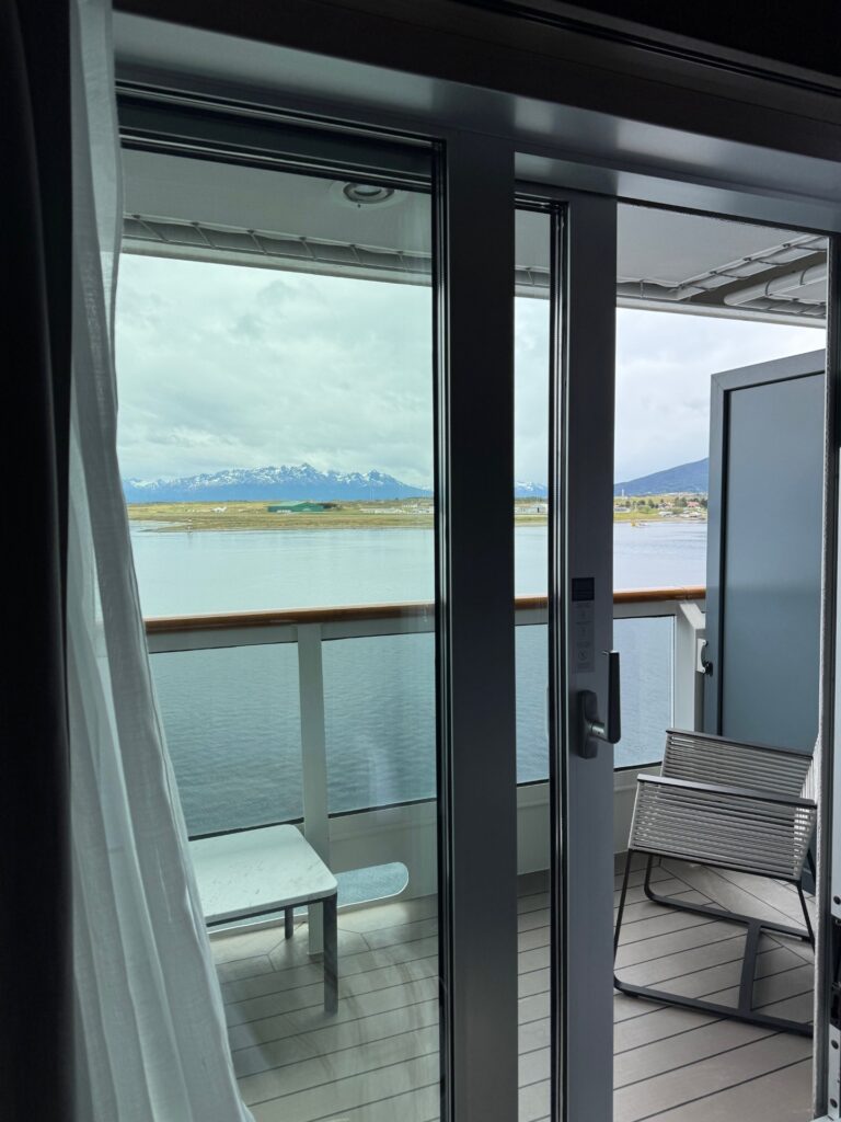 A chair and side table overlook the water and mountains of Ushuaia from the balcony of the room on the vessel.
