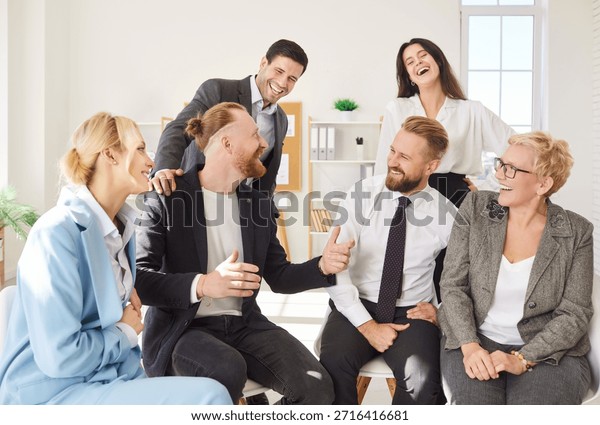 Cheerful group of colleagues sitting together in bright office, laughing and enjoying conversation. Happy smiling company employees having fun during team building activity. Corporate culture concept.